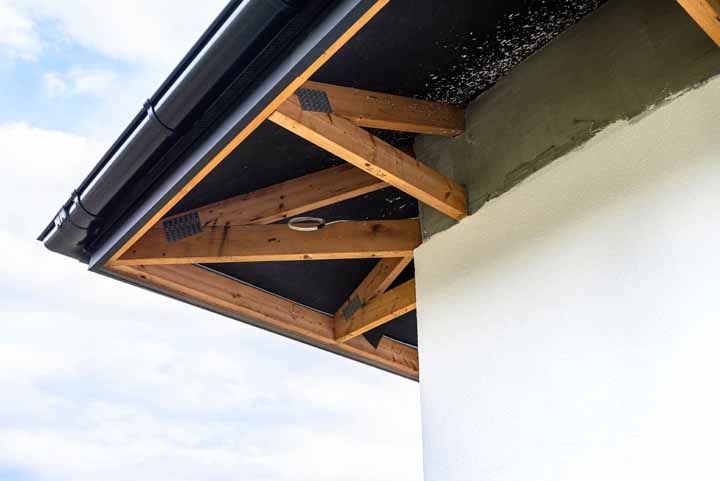 A newly applied layer of white silicone plaster on the wall of the house, visible roof trusses and a gutter.