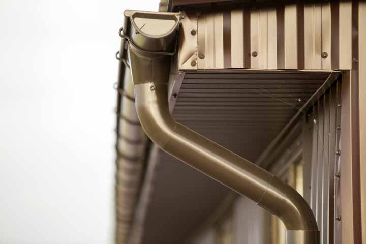 close up detail of cottage house corner with metal planks siding and roof with gutter rain system.